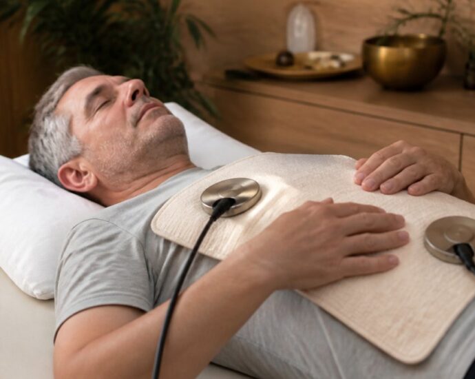 A man lying on a treatment table with two chest electrodes connected by wires for electrotherapy.