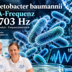 Acinetobacter baumannii – frekvence DNA 18 703 Hz – Herbert Eder – výzkumník v oblasti frekvencí Dva vědci v bílých polokošilích se usmívají do kamery před modrým vědeckým pozadím, na kterém jsou zobrazeny bakterie a nadpis s vlnovou křivkou o frekvenci 18,703 Hz (plakát o frekvenci DNA).