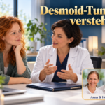 Desmoid-Tumor verstehen – Anna und Herbert - Herbert Eder - Frequenzforscher Fiktive rothaarige Patientin im ruhigen Gespräch mit einer fiktiven dunkelhaarigen Ärztin; auf dem Tisch liegt eine geschlossene Befundmappe. Porträtbadge Anna und Herbert rechts unten.