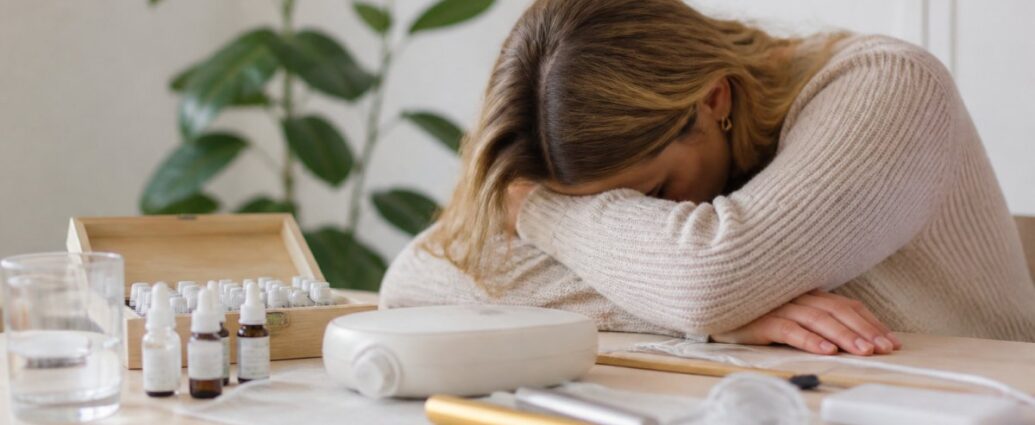 was-ist-informationsmedizin-bei-chronischer-erschopfung-1792215632 - Herbert Eder - Frequenzforscher Woman resting her head on her arms at a desk with essential oil bottles and a diffuser.