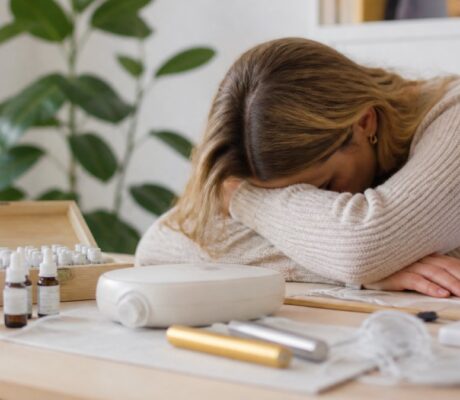 was-ist-informationsmedizin-bei-chronischer-erschopfung-1792215632 - Herbert Eder - Frequenzforscher Woman resting her head on her arms at a desk with essential oil bottles and a diffuser.